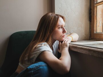 Junge Frau mit rötlichen Haaren schaut aus dem Fenster | © Getty Images/MementoJpeg