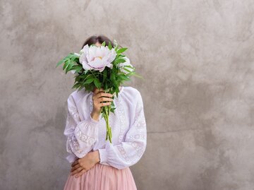 Junge Frau versteckt sich hinter Blumenstrauß | © GettyImages/	Alina Kostrytsia