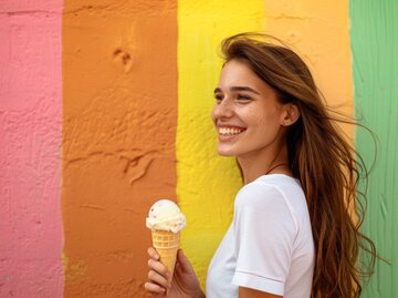 Junge Frau genießt Eiswaffel, bunten Hintergrund, glücklich und sorglos Moment, Sommer Leckerbissen, Spaß Atmosphäre Konzept | © Adobe Stock/Aksana/KI generiert