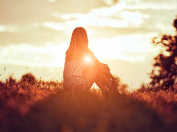 Silhouette einer Frau, die auf einem Feld sitzt. | © Adobe Stock/ astrosystem