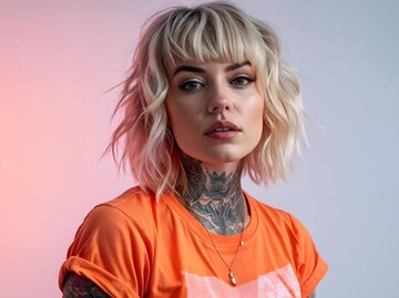 Junge schöne blonde Haare tätowierte Frau trägt einen Sommer orange farbigen T-Shirt auf hellrosa Farbe Hintergrund | © Adobe Stock/virtual_arts