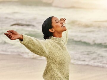 Frau mit ausgestreckten Armen am Strand | © Getty Images/Delmaine Donson