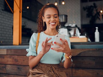 Frau lächelt und schaut auf ihr Handy | © Adobe Stock/Kay Abrahams/peopleimages.com