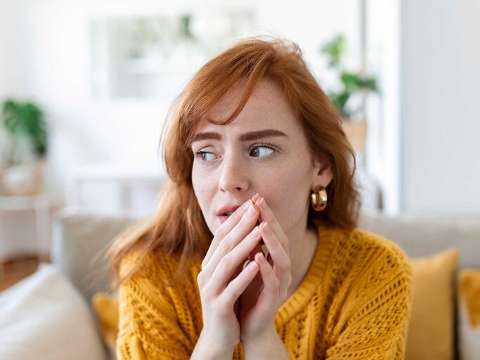 Frau mit roten Haaren grübelt und hält sich die Hände vor das Gesicht | © Adobe Stock/Graphicroyalty