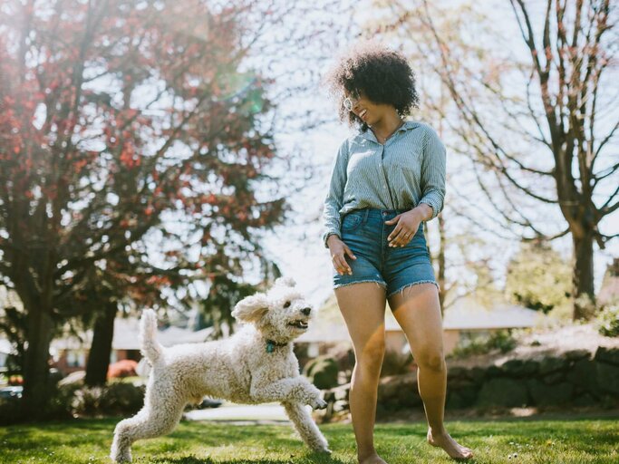 Person springt mit Hund über Wiese | © Getty Images/RyanJLane