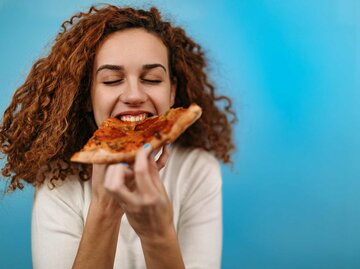 Frau beißt in ein Stück Pizza | © Getty Images/StefaNikolic