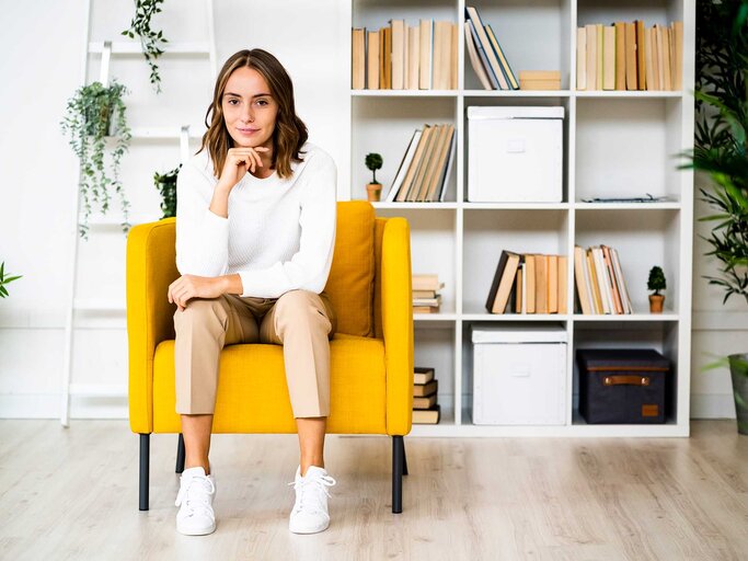 Frau sitzt seriös auf einer gelben Couch. | © Getty Images / Westend61