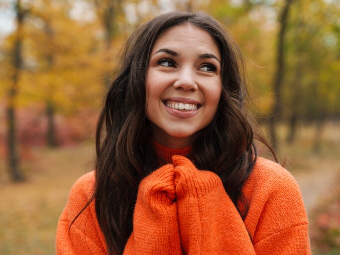 Lachende Frau in orangem Pullover vor Herbstlandschaft | © AdobeStock/Drobot Dean