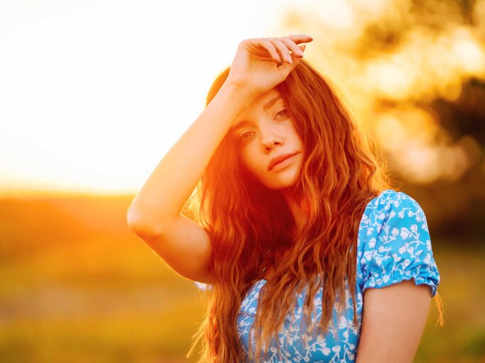 Junge Frau in stilvollem Sommerkleid fühlt sich frei auf dem Feld mit Blumen bei Sonnenuntergang. Natur, Mode, Urlaub und Lebensstil | © Adobe Stock/maxbelchenko