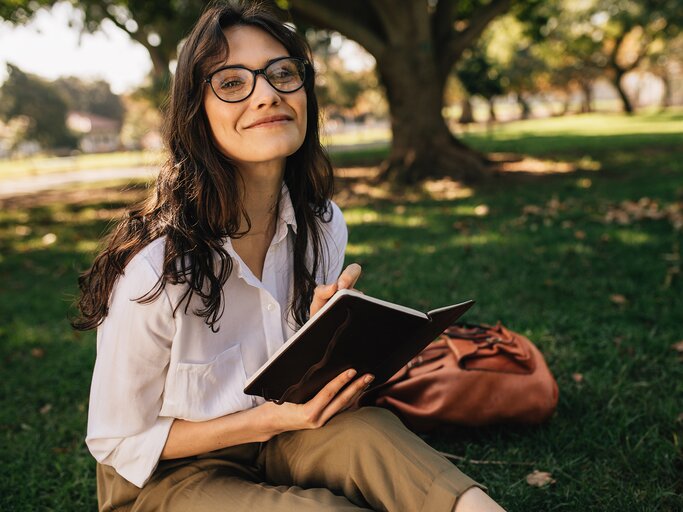 Eine Frau schreibt in ein Buch, im Park. | © Adobe Stock/Jacob Lund