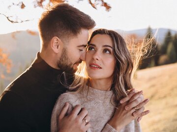 Stilvolles junges Paar in den herbstlichen Bergen. Ein Mann und eine Frau umarmen sich unter einem großen alten Baum vor dem Hintergrund eines Waldes und Berggipfeln... | © Adobe Stock/ AlexGukalovUkraine