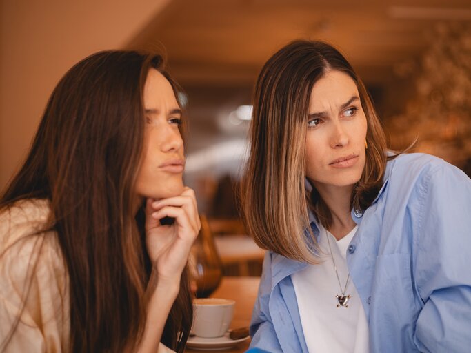 Zwei Frauen stecken die Köpfe zusammen und blicken neidisch nach rechts | © AdobeStock/zvkate