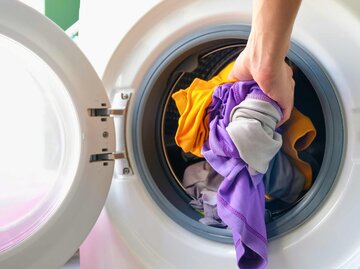 Hand steckt bunte Wäsche in die Waschmaschine | © Adobe Stock/Photo Sesaon