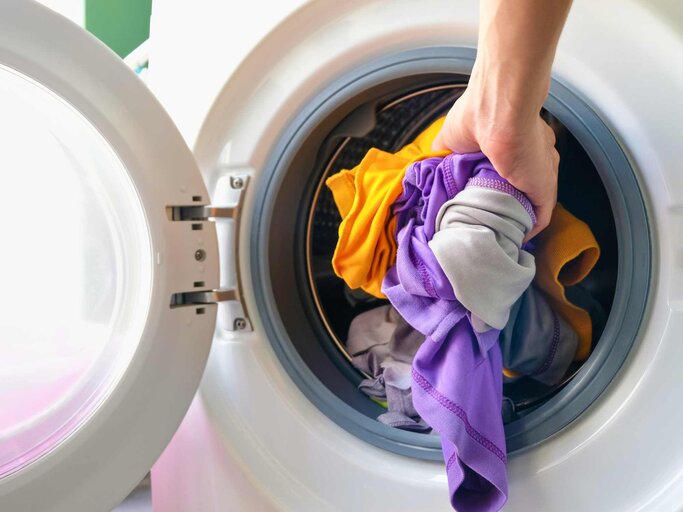 Hand steckt bunte Wäsche in die Waschmaschine | © Adobe Stock/Photo Sesaon