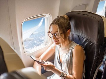 Frau sitzt im Flugzeug am Fenster | © Getty Images/RossHelen