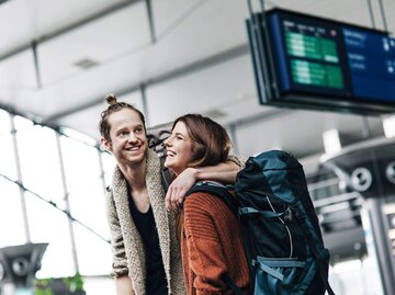 Paar mit Reiserucksäcken am Bahnhof | © Getty Images/Hinterhaus Productions