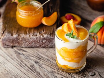 Ein Glas mit Sky-Aprikosen-Creme und einer Aprikosenhälfte als Deko | © Getty Images/Beton studio