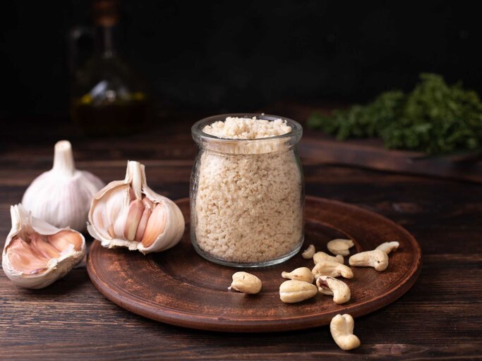 Cashewnuss-Parmesan im Glasgefäß mit Knoblauch auf Holzhintergrund, Nahaufnahme. | © Getty Images/Natalia Semenova