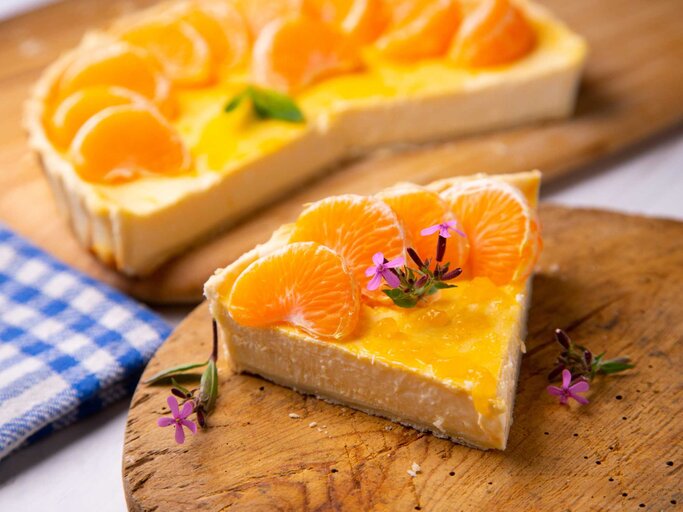 Ein Käsekuchen mit Mandarinen und Blumen auf einem Holzbrettchen | © Getty Images/Al Gonzalez