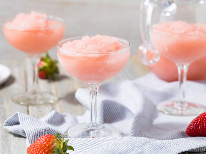 Gläser mit einem pinken Granita stehen auf dem Tisch, daneben liegen Erdbeeren.  | © Getty Images / bhofack2