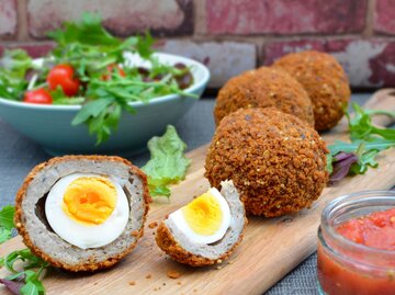 Scotch Eggs auf einem Brett mit Salatgarnitur | © Getty Images/gldburger