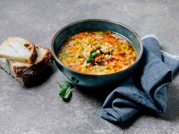 Gemüsesuppe mit Haferflocken auf einem Teller angerichtet mit etwas Brot daneben | © Getty Images/Claudia Totir