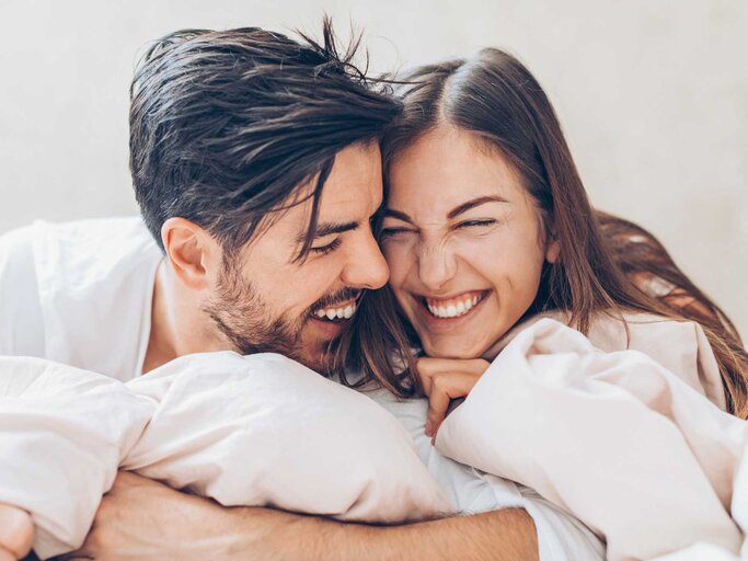 Mann und Frau liegen zusammen im Bett und lachen | © Getty Images/pixelfit