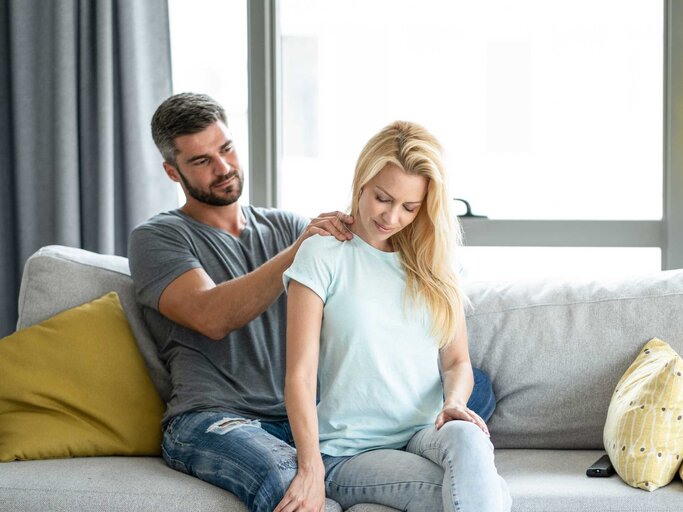 Mann massiert seiner Frau im Wohnzimmer die Schultern. | © Getty Images/DjelicS