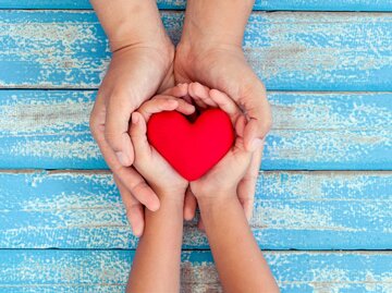 Hände von Frau und Kind halten ein rotes Herz. | © Getty Images/Sasiistock