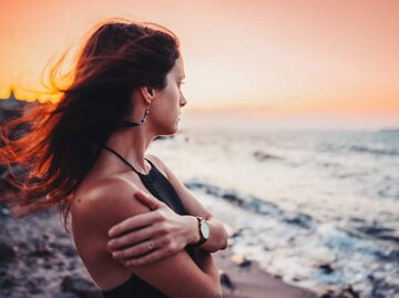 Frau steht bei Sonnenuntergang am Strand | © Getty Images/martin-dm