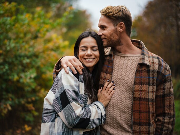 Frau und Mann in karierten Hemden spazieren Arm in Arm durch herbstliche Landschaft | © AdobeStock/Drobot Dean