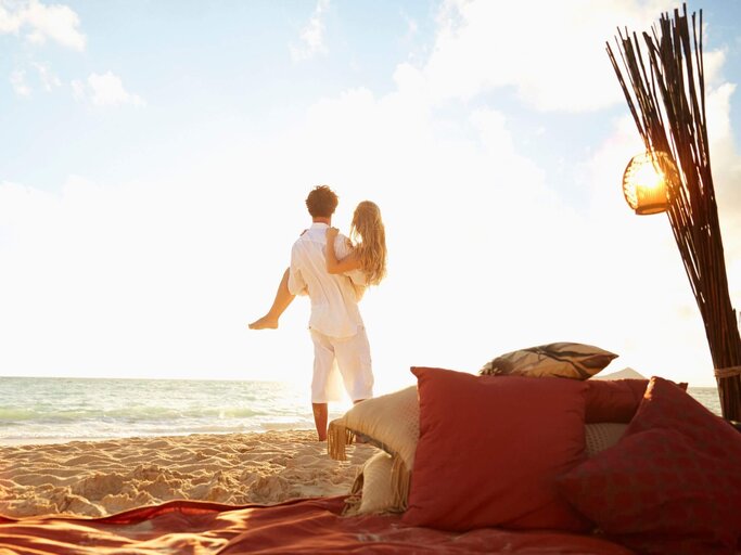 Mann trägt Frau auf Händen am Strand in Flitterwochen | © Getty Images/Colin Anderson Productions pty ltd