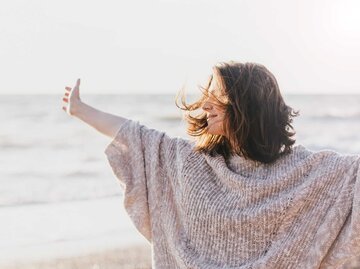 Junge Frau am Strand breitet die Arme aus | © Adobe Stock/polinaloves