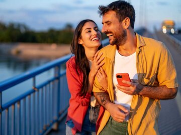 Mann und Frau spazieren lächelnd über eine Brücke | © Getty Images/RealPeopleGroup