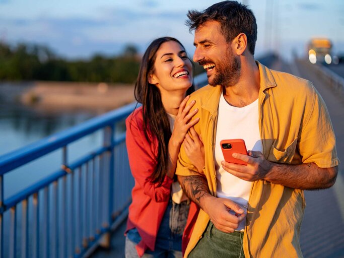 Mann und Frau spazieren lächelnd über eine Brücke | © Getty Images/RealPeopleGroup