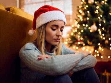 Frau schaut bedrückt zu Boden und trägt eine Weihnachtsmütze | © Adobe Stock/Drazen