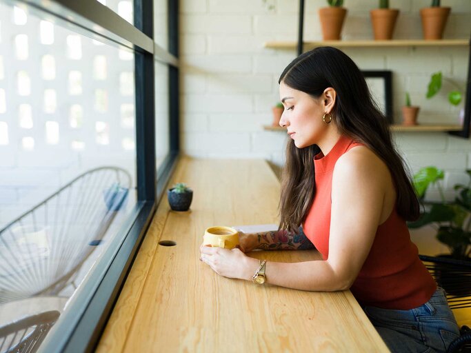 Single-Frau sitzt alleine im Café und schaut betrübt auf ihre Tasse in den Händen. | © Adobe Stock/AntonioDiaz