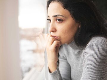 Nachdenkliche Frau blickt aus dem Fenster | © Adobe Stock/ARAMYAN