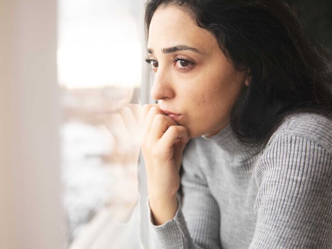 Nachdenkliche Frau blickt aus dem Fenster | © Adobe Stock/ARAMYAN