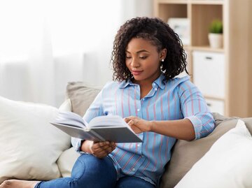 Frau sitzt auf dem Sofa und liest | © Adobe Stock/Syda Productions