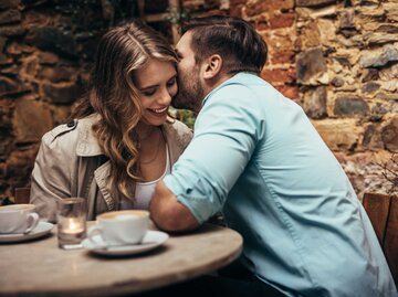 Mann flüstert seiner Partnerin im Cafe etwas zu. Sie lächelt. | © Adobe Stock/Jacob Lund