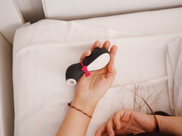 Die Hände einer Frau halten im Bett einen Vibrator in Pinguin-Optik. | © Adobe Stock/andrey