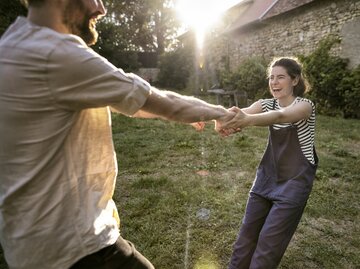 Frau hält sich an den Händen ihres Mannes fest, während sie im Garten herumalbern | © GettyImages/Oliver Rossi