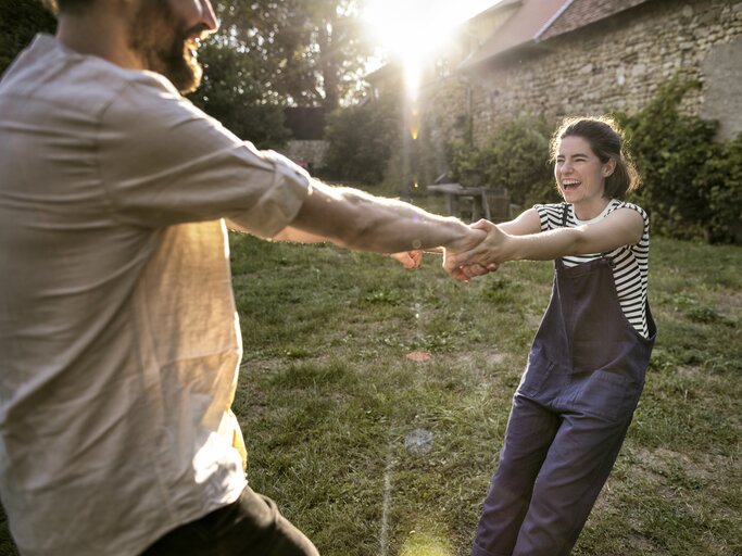 Frau hält sich an den Händen ihres Mannes fest, während sie im Garten herumalbern | © GettyImages/Oliver Rossi