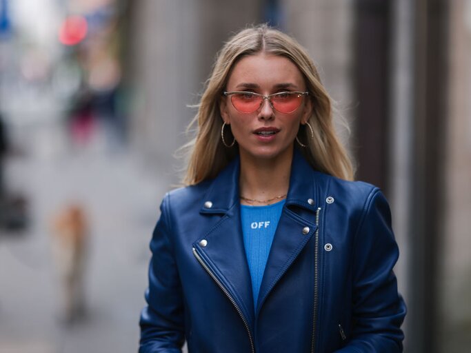 Junge Frau trägt blaue Lederjacke, blaues Top und rosa Sonnenbrille | © Getty Images/Jeremy Moeller 