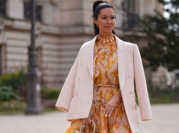 Frau trägt orangenes Blumenkleid und cremefarbenen Blazer | © Getty Images/Edward Berthelot 