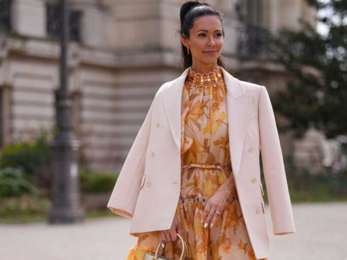 Frau trägt orangenes Blumenkleid und cremefarbenen Blazer | © Getty Images/Edward Berthelot 