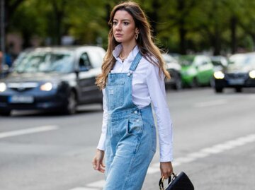 Frau trägt eine Jeans-Latzhose über einer weißen Bluse | © Getty Images/Christian Vierig