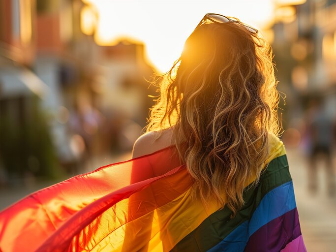 Frau mit Regenbogenflagge über den Schultern in der Sonne | © AdobeStock/Kazmi