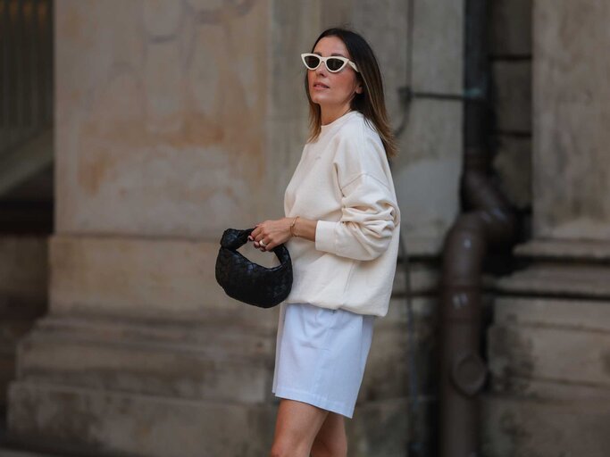 Frau trägt einen beigen Sweater, eine weiße Sonnenbrille und blaue Shorts | © Getty Images/Jeremy Moeller